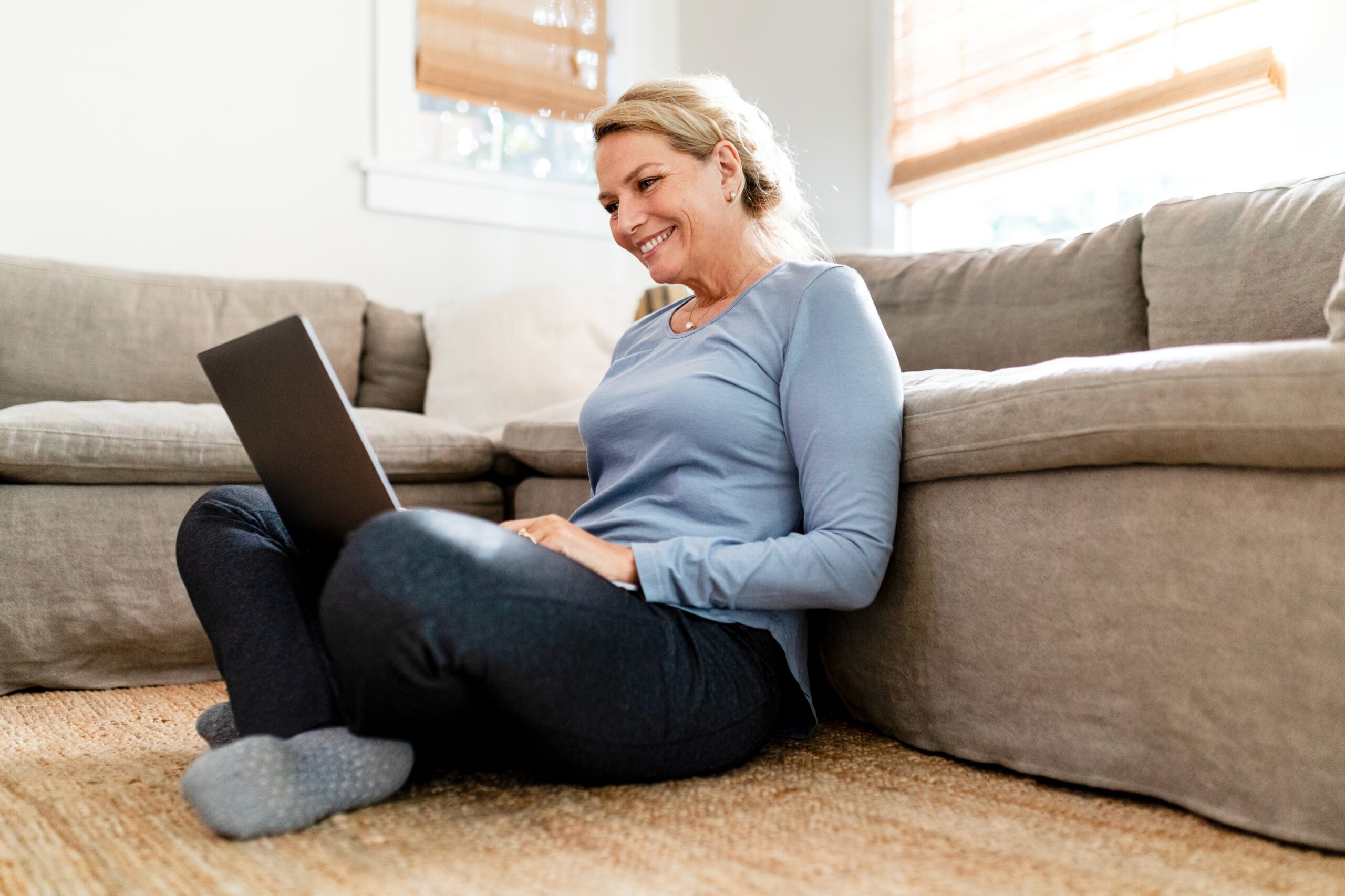 Mature woman using laptop, sitting on the living room's floor at home